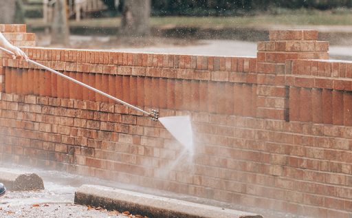 a home's brick wall being power washed from a Grime Stoppers technician