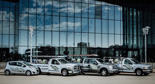 Four vehicles in various styles with the Grime Stoppers logo on them in front of a building with glass windows.