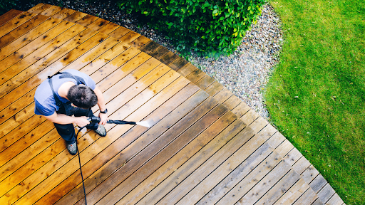 An aerial view of a man pressure washing a large wood surface on the ground.